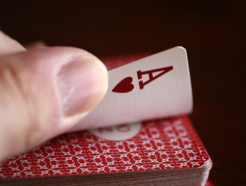 Person's hand over a deck of cards, peeling back the top card, which is an Ace of hearts.