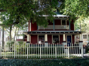 a deep red-colored house with a white picket fence and a large tree out front